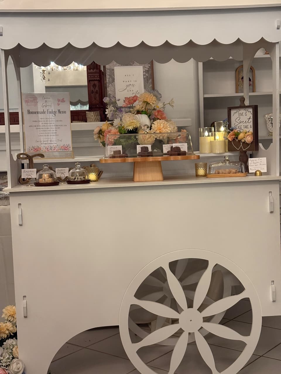 Close view of the handcrafted white fudge cart, with a flower arrangement, candles, menu, and fudge display